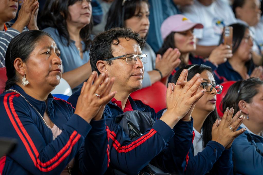 A group of diverse individuals clapping and showing support in a crowded setting, wearing matching jackets with red stripes.